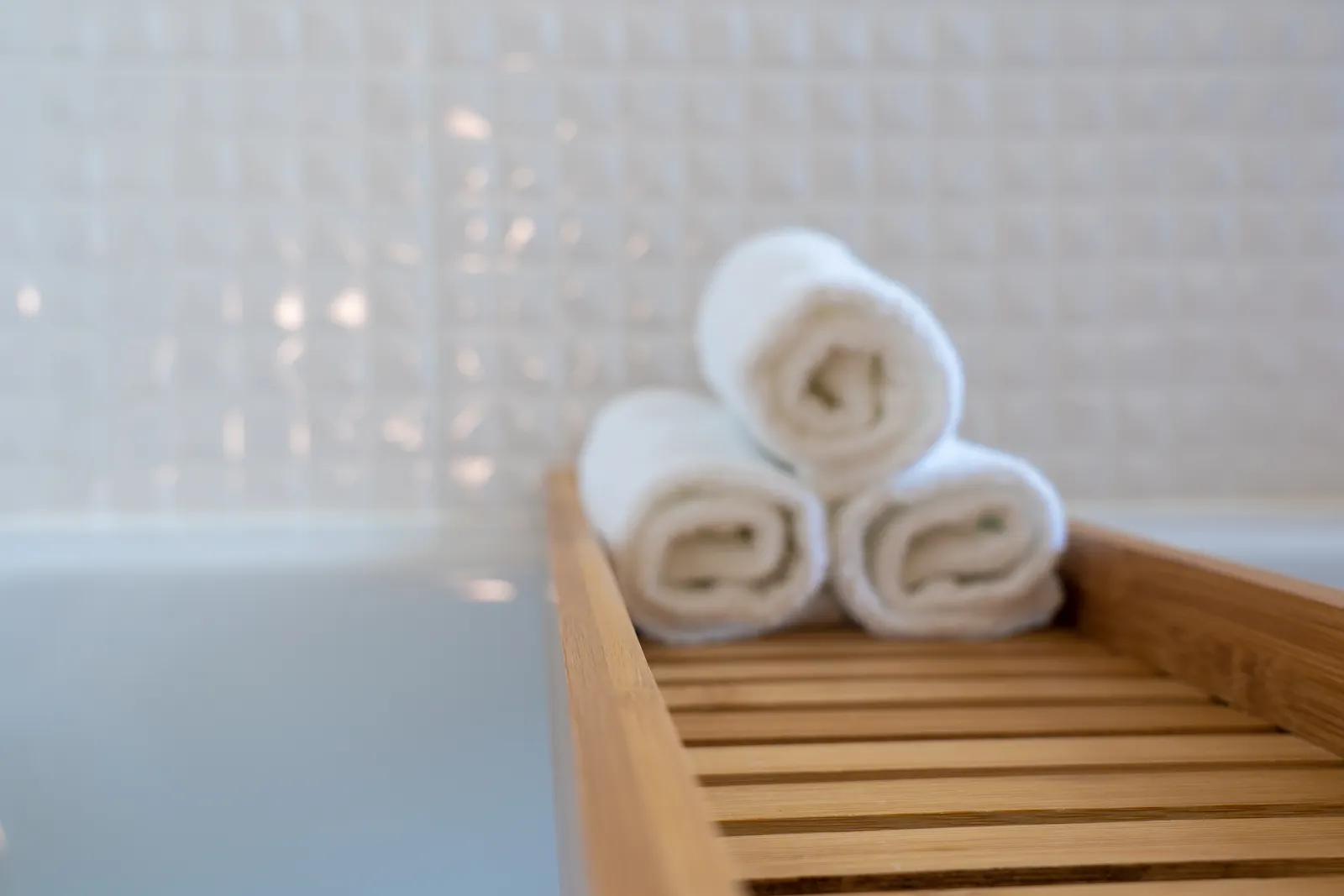 Rolled white towels on a wooden bath tray in a modern spa bathroom